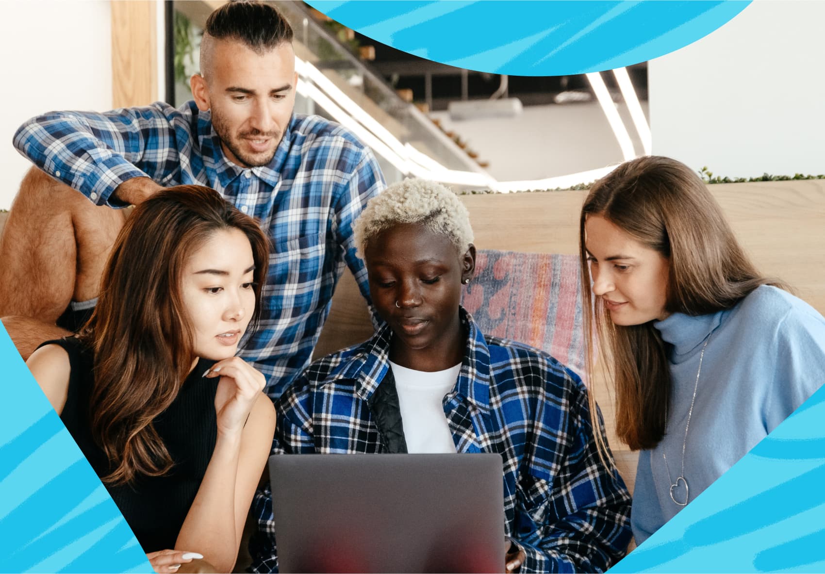 A woman sitting in front of a laptop at work with three co-workers sitting next to her looking over her shoulder