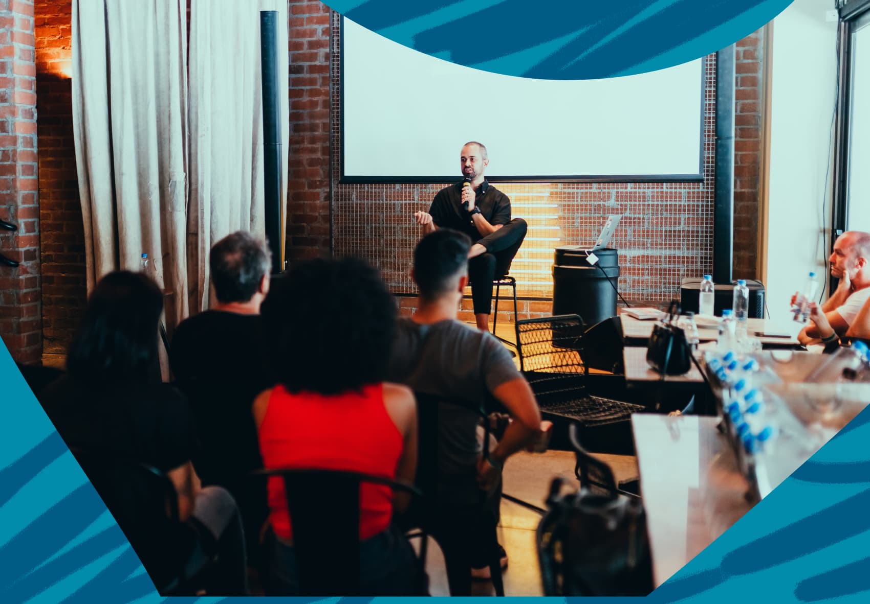 Man sitting on a small stage with a microphone, speaking to a group of people at a conference